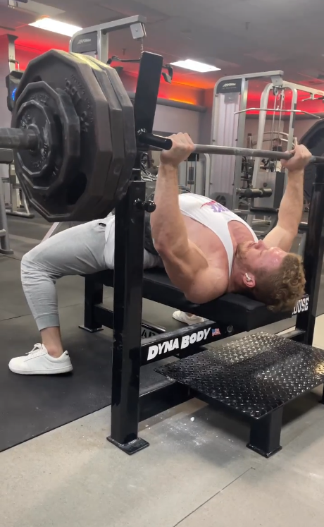 Person performing a bench press with weights in a gym setting wearing Icarus Ascent Gen 2 in barefoot shoe in white/red