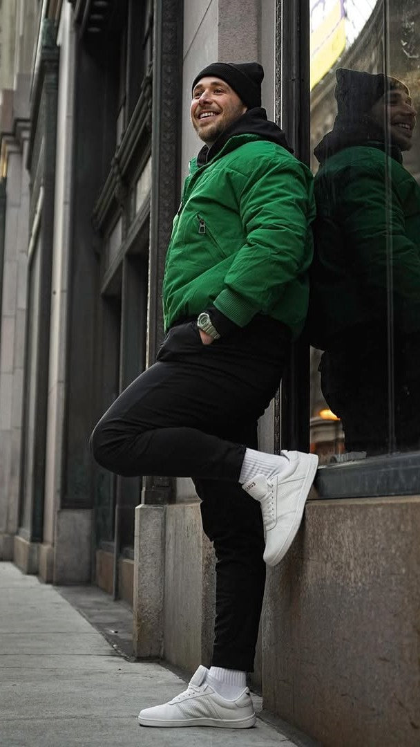 Man in green jacket and black pants leaning against a building wall, wearing Icarus Ascent white/red sneaker