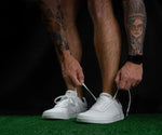 Load image into Gallery viewer, Tattooed man lacing up Icarus Ascent shoe laces on a turf surface inside a gym.
